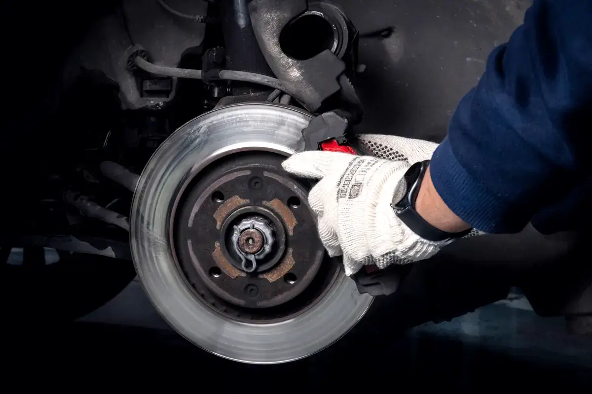 Gehandschoende hand aan een remschijf en remklauw onder de auto